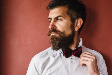 The man on the background of a burgundy wall looks angrily raising his eyebrows.