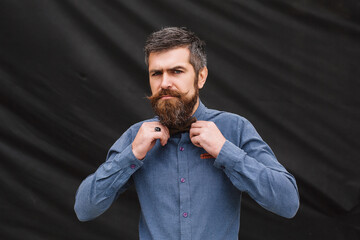 A man in despair on a black background fixes his bow tie.