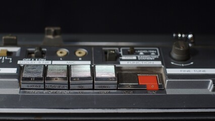 A finger presses several buttons on an old vintage cassette recorder: play, rewind, fast forward, stop, rec