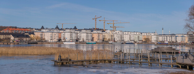 Fototapeta na wymiar Panorama view at the icy bay Hammarby sjö with floes, apartment building and recreation area with commuting ferries a sunny winter day in Stockholm