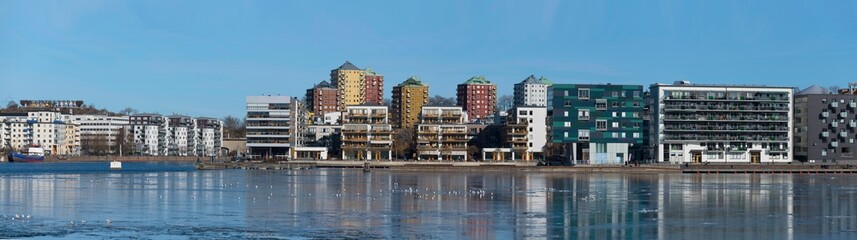 Panorama view at the icy bay Hammarby sjö with floes, apartment building and recreation area with...