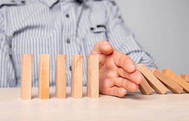 Business crisis and risk protection concept. Businessman hand closeup protecting wood blocks from falling. Insurance strategy. Domino effect stopping. High quality photo