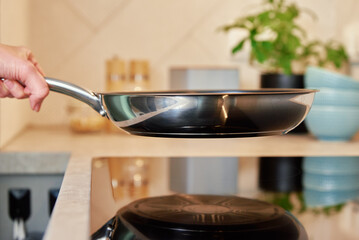 Woman hold steel frying pan on induction stove in the kitchen, Modern kitchen appliance