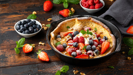 Dutch baby pancake with berries and icing sugar in a iron cast pan. Morning breakfast