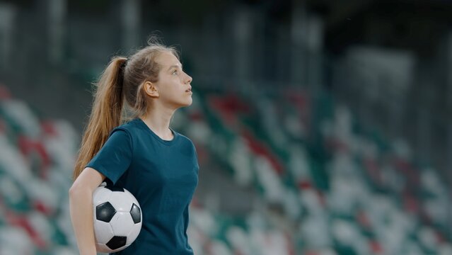 Portrait of Caucasian pre teen girl entering the field of huge soccer stadium, holding a ball, dreaming of becoming professional player, soccer star