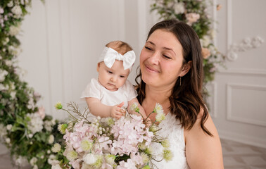 portrait of a Caucasian brunette mom with a bouquet of flowers holding a baby daughter