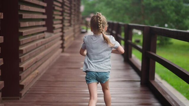 Little girl with blonde plait runs along empty veranda deck