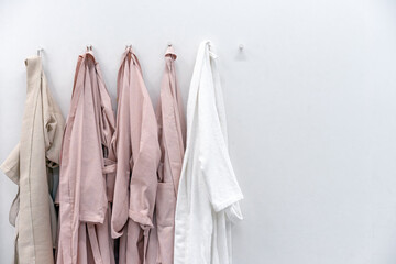 White and beige bathrobes on hooks in the bathroom. Home wear.