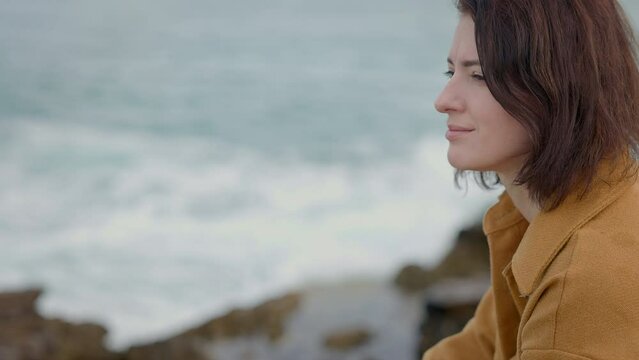 Young Woman By Sea. She Sits And Stares Dreamily At Sea. Romantic Image.
