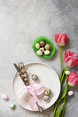 Obraz na płótnie Canvas Festive Easter table setting with painted eggs, spring flowers and cutlery on light grey tabletop. Table setting for Happy Easter day.