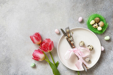 Festive Easter table setting with painted eggs, spring flowers and cutlery on light grey tabletop. Table setting for Happy Easter day.