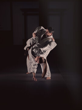 Young Judo Practitioners Showing Sweeping Hip Throw Technique In Black Studio