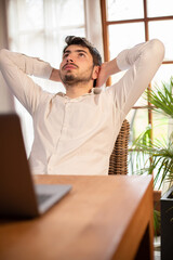 portrait d'un jeune homme qui se détend et s'étire devant son ordinateur. Il se repose dans son...