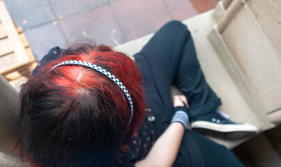 Punk emo girl, young adult with black red hair, sitting at a window frame, looking down, high angle view, horizontal