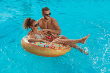 Happy couple with inflatable ring in outdoor swimming pool on sunny summer day