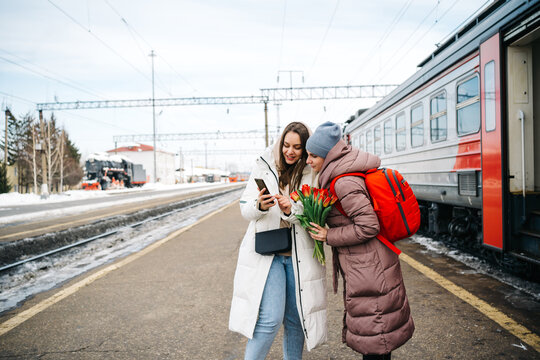 two girls on the station platform with flowers happily looking into a smartphone