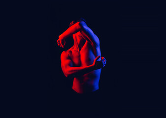 Fashion art photo of a strong young beautiful sexy body of an athlete in red and blue tones of neon light on an isolated dark background in colored spotlights.