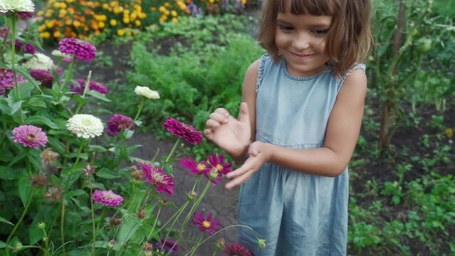 Happy little girl rejoices in the flowers in the garden. Funny Kid touches flowers with his hands, wants to pick a bouquet of flowers