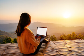 Young woman freelancer traveler working online using laptop and enjoying the beautiful nature landscape with mountain view at sunrise