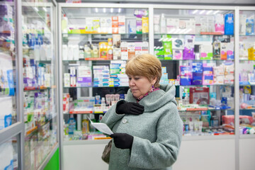 Elderly woman in   coat buys medicines at   pharmacy