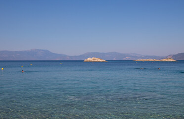 Fototapeta na wymiar Seascape, greek beach with clear mediterranean sea, bathing people and small island, Greece