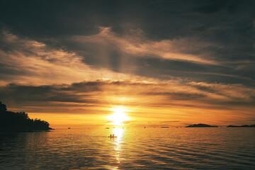 Fototapeta premium Dramatic sunset over sea with clouds in the sky and canoe rider in the foreground - Thailand Koh Lipe