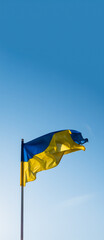 Ukrainian flag vertical banner, empty copy space. Flag of Ukraine on blue sky background. National symbol of freedom and independence. "Slava Ukraini!" (Glory to Ukraine).