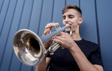 Young street musician playing the trumpet near the big blue wall