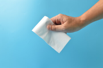 Hand holding white paper tissue isolated on a blue background. Hygiene, safety and healthcare concept.