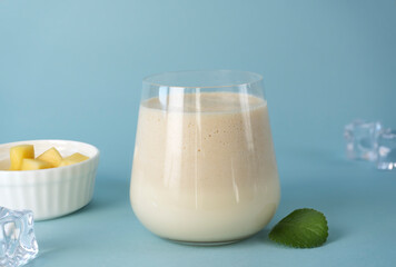 Glass of traditional Indian lassi drink with mango and ice on a blue background.