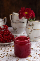 Healthy jam from viburnum berries (Viburnum opulus) in a glass jar, a bunch of viburnum, antique dishes and chrysanthemums in a vase. Preparations for the winter from colds