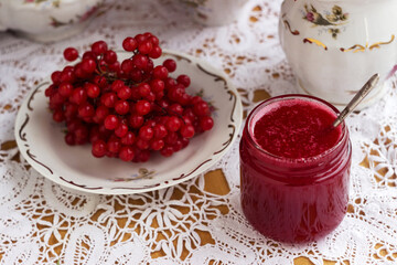 Healthy jam from viburnum berries (Viburnum opulus) in a glass jar, a bunch of viburnum, antique dishes and chrysanthemums in a vase. Preparations for the winter from colds
