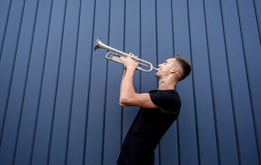 Young street musician playing the trumpet near the big blue wall