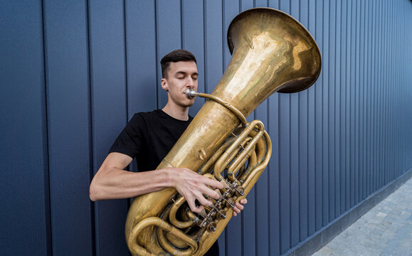 Young street musician playing the tuba near the big blue wall
