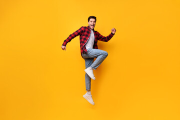 Fototapeta na wymiar Excited young man jumping up at orange studio