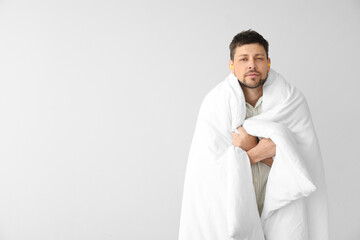 Handsome man with ear plugs and blanket on light background