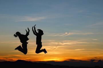 Silhouette of happy two children girls jumping on mountain sunset background.