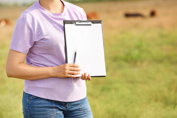 Woman with clipboard and pen on pasture
