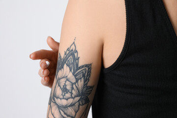 Woman applying cream onto her arm with tattoo on white background, closeup