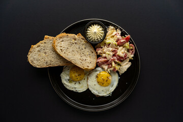 Breakfast, fried eggs on a black plate with tomatoes and chili peppers with bread on a black background