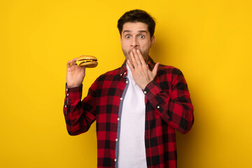 Funny Young Guy Holding Burger And Covering Mouth