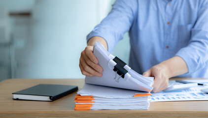 The office worker is working at the company, he is tidying up the paperwork on his desk to start working on the paperwork, he is in the finance department and is preparing the financial statements.