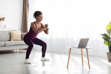 Fototapeta na wymiar Positive black lady exercising at home, watching online video