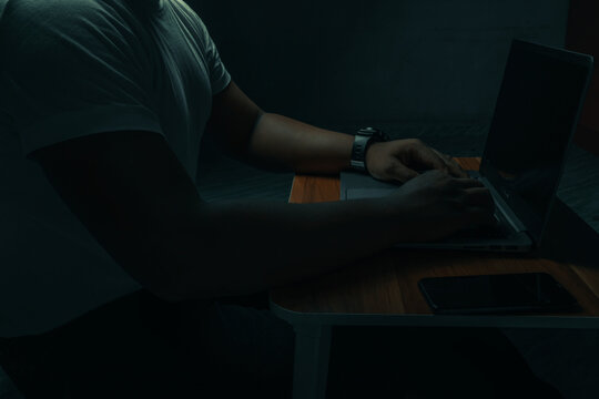 A man in a white shirt sits on a laptop in a dark room. with light shining down. internet concept addiction.topview.