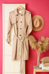 Stylish trenchcoat hanging on folding screen near pink wall in hall