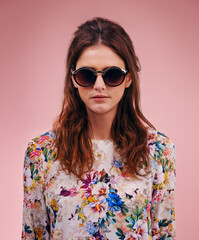 Stunning and stylish. Portrait of an attractive young woman wearing designer shades against a pink background.