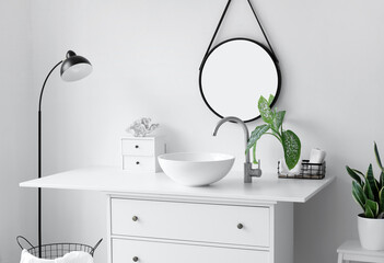 Modern sink with houseplant, drawers and standing lamp near light wall