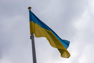 Big flag of Ukraine on a high flagpole against a cloudy sky.