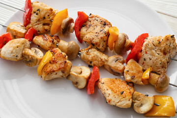 Plate of grilled chicken skewers with vegetables on table, closeup