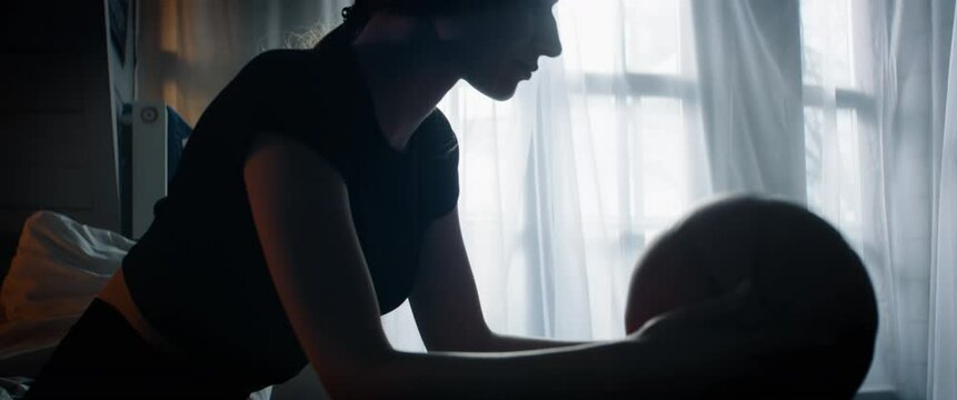 CU Silhouette of bored Caucasian teenager girl playing with basketball ball in her attic bedroom at home. Shot with 2x anamorphic lens